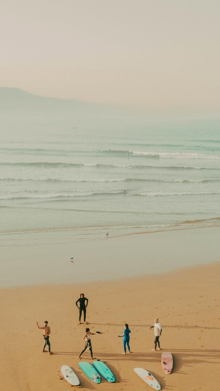 A group warming up on a wide, hazy beach with soft-top boards laid out on the sand