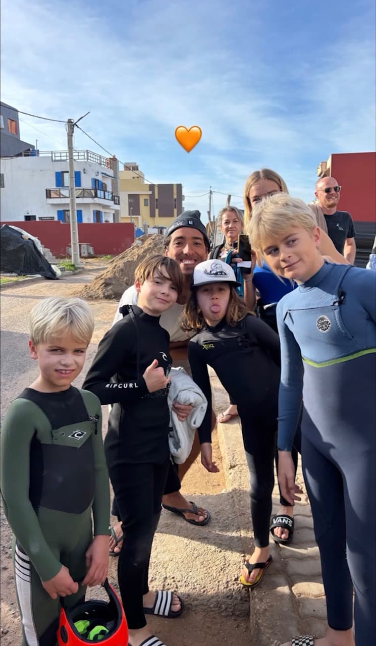 The coach with a group of young surfers in wetsuits gathered together after a session in the village